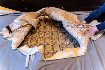 A man cut a spring mattress with a knife. Spring block and foam lining