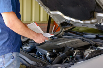 Man holding and reading the car user manual or user instruction to checking or fixing engine of...
