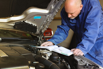 Mechanic man holding and reading the car user manual or user instruction to checking or fixing...