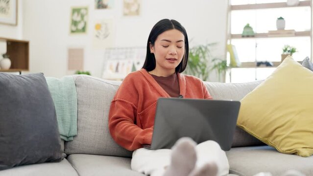 Remote work, smile and Asian woman on sofa with laptop for working online, research and planning. Freelancer, home and happy girl on couch on computer to browse internet, typing email and relaxing