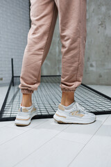 Sports shoes for women. Slender female legs in pants and white stylish casual sneakers. Women's comfortable summer shoes.