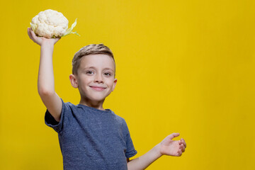 Cauliflower in the hands of a cheerful boy on a yellow background. Healthy food