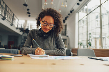 Attractive young female student studying and making notes in modern coworking