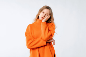 Bored woman thinking, looking complicated, dreaming of something, standing in soft orange sweater over neutral studio background