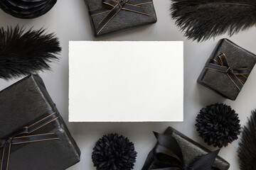 Blank card between Wrapped Gift Boxes, black paper flowers and feathers, mockup