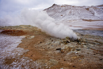 geyser , fumerole, vapeur et souffre avec de la terre ocre devant une montagne enneigé 