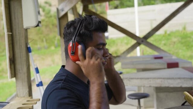 Male Shooter Puts On Ear Muffs At The Firing Range. side view