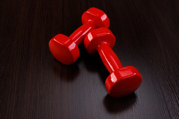 A pair of red dumbbells lies on a wooden glare surface. Angle view. Selective focus.