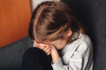 Fototapeta premium Little girl crying and hiding at her room. Child covering head with hands while suffering from domestic violence at home.