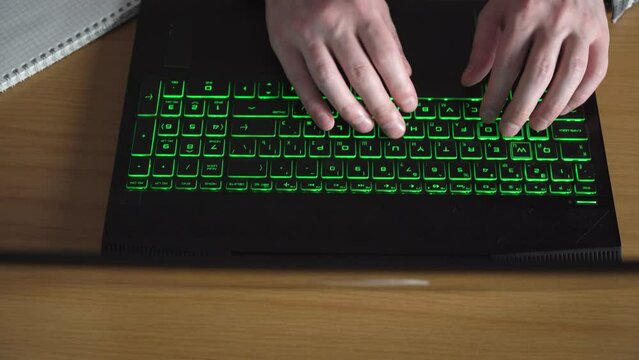 a man is typing text on a laptop keyboard with green backlight. slide