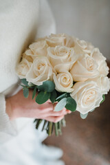 Beautiful bouquet of white roses, and eucalyptus leaves. A young beautiful girl in an elegant dress is standing and holding hands a vintage bouquet of flowers and greens. Closeup details. Top view.