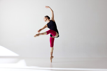 One flexible ballerina wearing pointe shoes dancing with closed eyes over white background © Lustre Art Group 