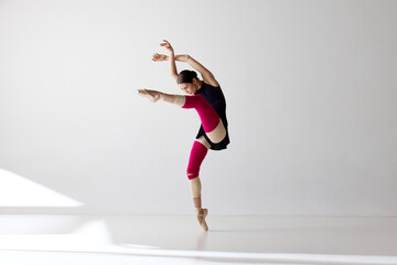 Young beautiful ballerina wearing pointe shoes dancing and looking away over white background © Lustre Art Group 