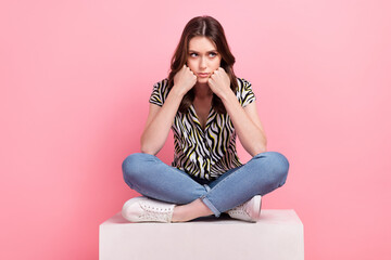 Full length photo of capricious young person sit podium hands touch cheeks look empty space isolated on pink color background - obrazy, fototapety, plakaty