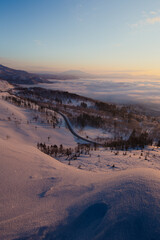 雪に覆われた斜面の下に雲海が広がる冬の夜明け。日本の北海道の美幌峠の風景
