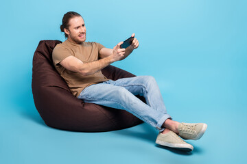 Full length photo of cheerful pretty man wear beige t-shirt bean bag watching video gadget emtpy space isolated blue color background - obrazy, fototapety, plakaty
