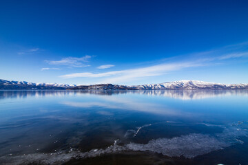 爽やかな青空と鏡の湖面、遠くに雪山を見る晴れた冬の日の湖。日本の北海道の屈斜路湖。