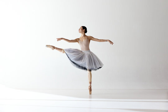 Young graceful woman ballet dancer dressed in professional outfit, shoes and white weightless skirt demonstrating dancing skill. Beauty of classic ballet