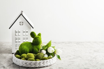 Close up Easter bunny rabbit statuette and basket with tulips and house on green grass lawn...