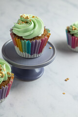Three carrot cupcakes, with green frosting, one on a purple pedestal.