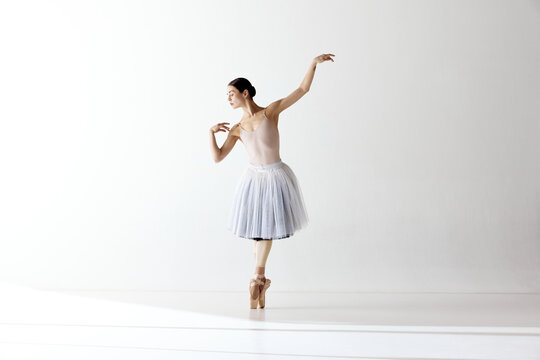 Ballerina dancing graceful movement in dress over white background. Beauty of classic ballet