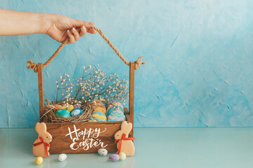 Wooden basket with Easter eggs and sweets on the table. An ordinary kitchen room with flowers in a pot. Easter concept.