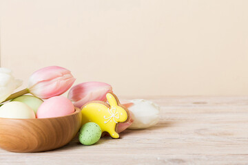 Happy Easter composition. Easter eggs in basket on colored table with yellow Tulips. Natural dyed colorful eggs background with copy space