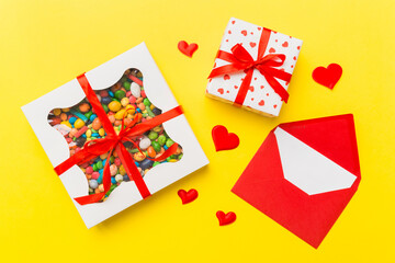 Red envelope with candy and gift box and Valentines hearts on colored background. Flat lay, top view. Romantic love letter for Holiday concept
