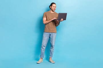 Full length photo of cute positive man wear beige t-shirt communicating modern gadget isolated blue color background