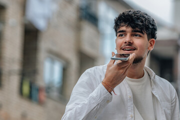 young man in the street with phone sending voice message or recording audio