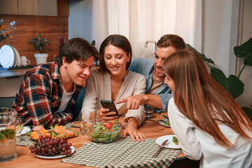 Using smartphone. Group of people are on the kitchen, having dinner, spending time together