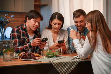 Using smartphone. Group of people are on the kitchen, having dinner, spending time together