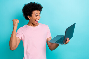 Photo of youth overjoyed crazy guy fist up pink t-shirt hold netbook celebrate victory millionaire gambling isolated on aquamarine color background