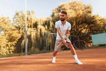 Active training. Young man is on the tennis court at sunny daytime