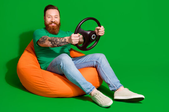 Full length photo of positive good mood man wear t-shirt sitting bean bag riding auto empty space isolated green color background