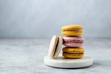 Stack of yellow, pink and ivory colored macaron cookies on a white marble stand. French mini...