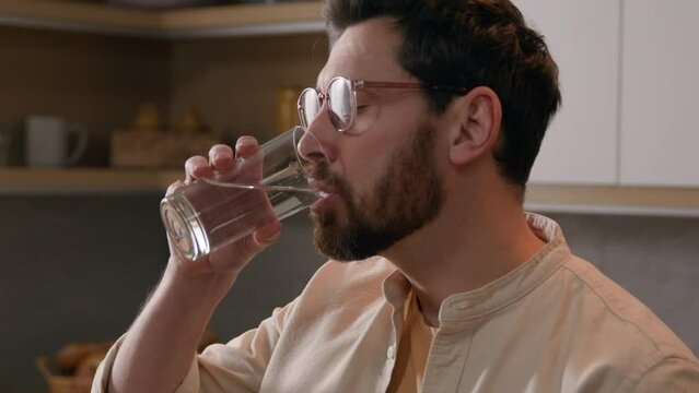 Moving shot Caucasian man freelancer businessman male at kitchen at home working remote computer browsing chatting laptop drinking glass of water thirty guy drink refreshment aqua delivery service