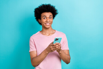 Portrait photo of young funny guy chevelure hairdo wear pink t-shirt hold his samsung galaxy phone browse website isolated on cyan color background