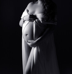 A pregnant woman in a white dress on a black background. Studio pregnancy photo shoot. Space for text.