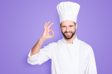 Portrait of cheerful joyful chef cook in beret and white outfit with stubble looking at camera...