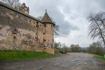 Old walls of Ronneburg Castle with a round tower and street in front during cloudy day, Germany