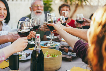 Happy family cheering with red wine at barbecue dinner outdoor - Focus on right female hand