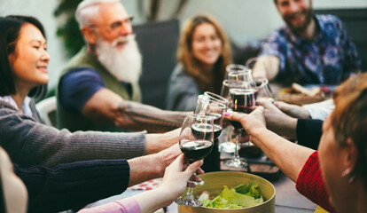 Multiracial happy friends cheering with red wine at barbecue dinner outdoor - Focus on left female hand