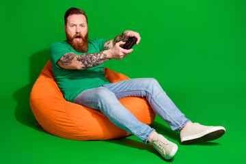 Full length photo of impressed funky guy dressed t-shirt enjoying playstation emtpy space isolated green color background - obrazy, fototapety, plakaty