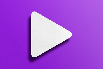 White paper cut into triangle shape, play button set on purple paper background.