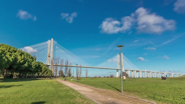The Vasco da Gama Bridge timelapse hyperlapse with green lawn and trees. Cable-stayed longest bridge flanked by viaducts and rangeviews that spans Tagus River in Park of Nations in Lisbon, Portugal