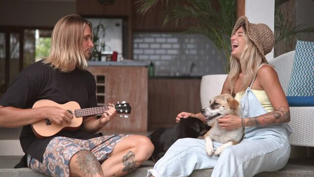 Loving family sing fun song. Happy talent man play ukulele guitar. Joyful people care cute street dogs. Lovers couple rest together. Hippies romantic date. Pets sit porch. Guitarist concert performing