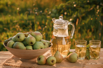 Two glasses with pear juice and basket with pears on wooden table with natural orchard background on sunset light. Vegetarian fruit composition