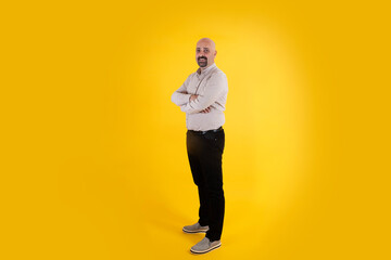 Full body portrait of man, bald middle aged smiling full body portrait of man. Isolated yellow background, copy space. Casual dressed positive father figure male, arms crossed. Proud, confident guy. © Designerant