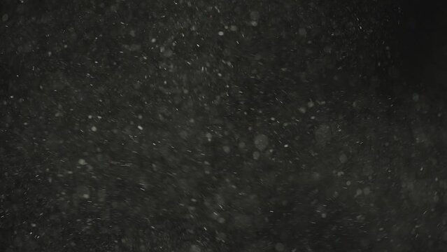 Slow motion real dust particles explosion and flow in the air with natural sunlight over black background